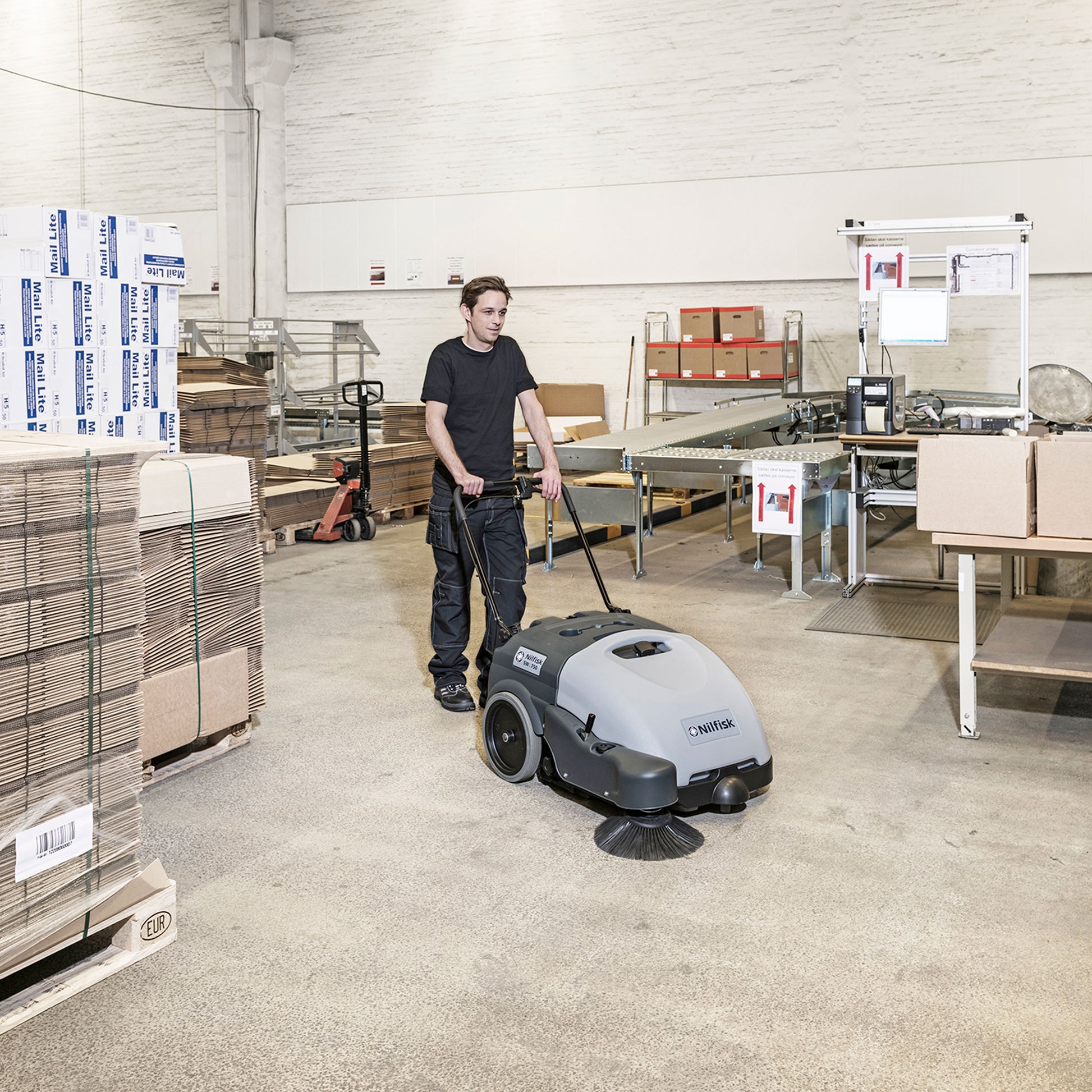 Nilfisk SW750 batteridrevet fejemaskine med sidekost, ergonomisk håndtag og kompakt design til professionel rengøring af lager, værksteder og erhverv