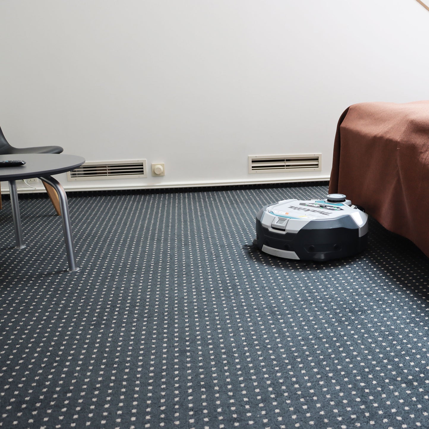 Robotstøvsuger i hvidt/gråt hus på gulv, set fra siden med børster