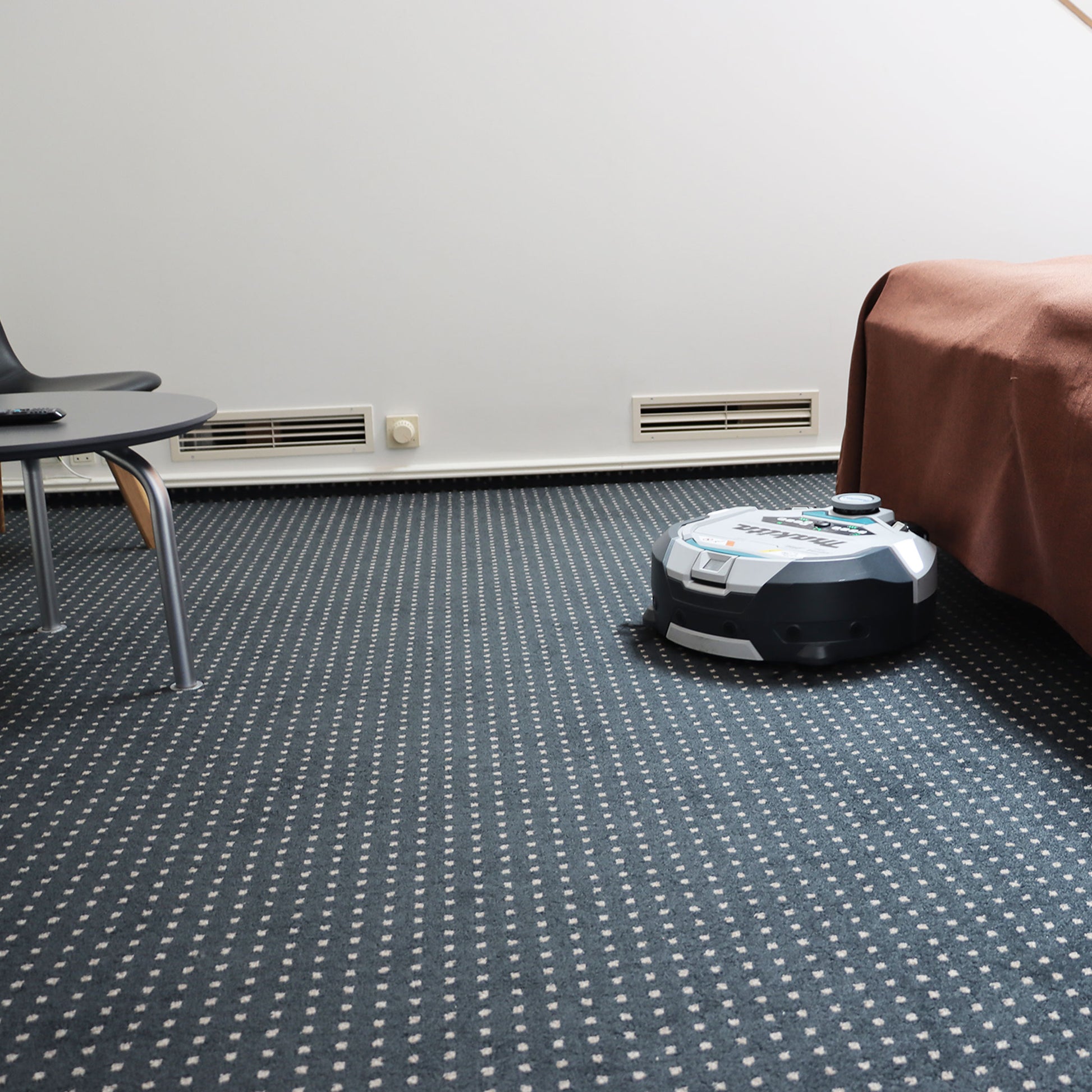 Robotstøvsuger i hvidt/gråt hus på gulv, set fra siden med børster